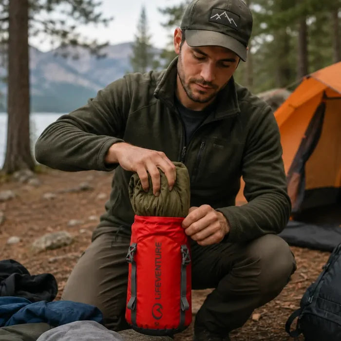 Man camping in the wild stuffing a garment into a Lifeventure Ultralight Compression Sack 5 Litres red