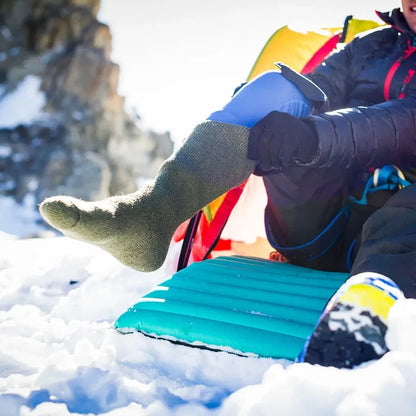 Lifestyle image of a man putting on a pair of Sub Zero long walking socks whilst camping in the snow