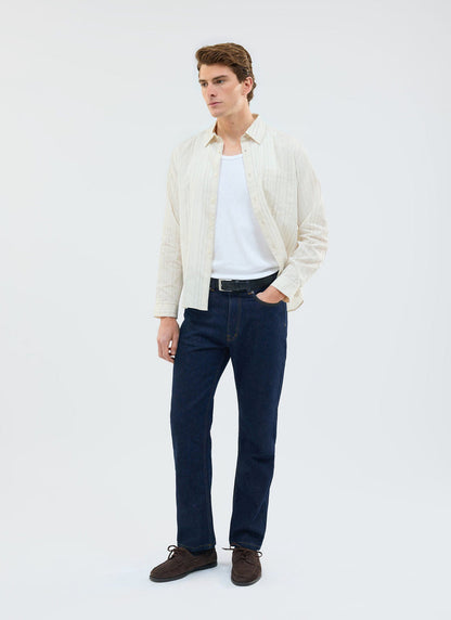 A model wears the ecru Lorenzo Pearce Shirt by Percival, styled open over a white vest and dark blue jeans.