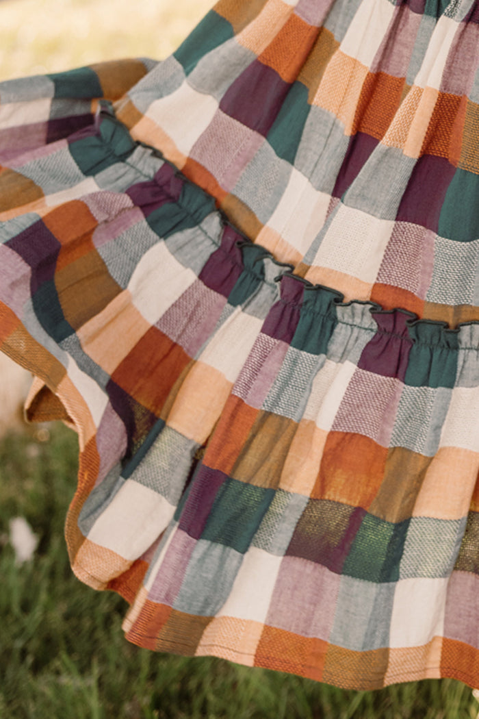 A close-up of the Madeline Skirt in Maize Gingham by Ivy City Co, a flowing cotton-blend skirt featuring a vibrant plaid pattern in orange, green, purple, and cream—pictured outdoors on grass.
