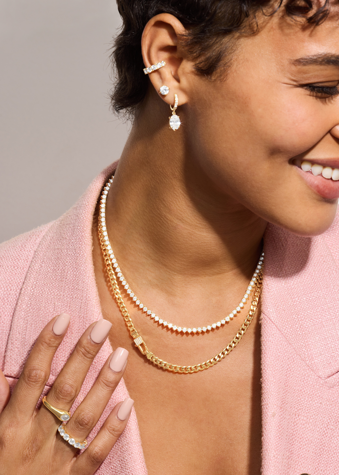 Woman wearing a gold chain necklace with a lock clasp and pave accents and other jewelry