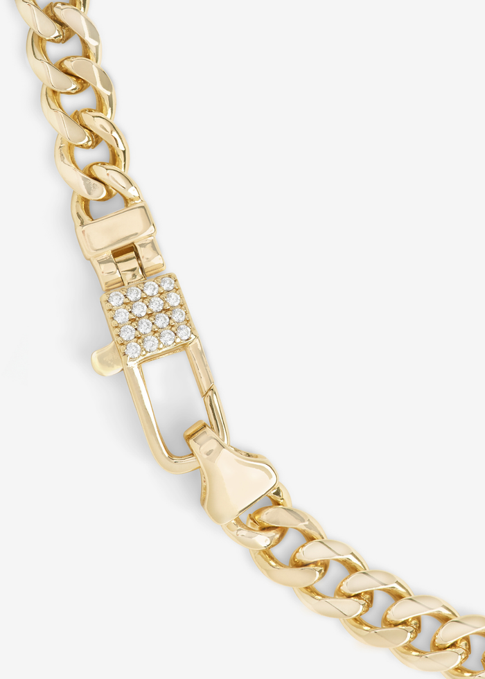 Close up of a gold chain necklace with a lock clasp and pave accents on a white background