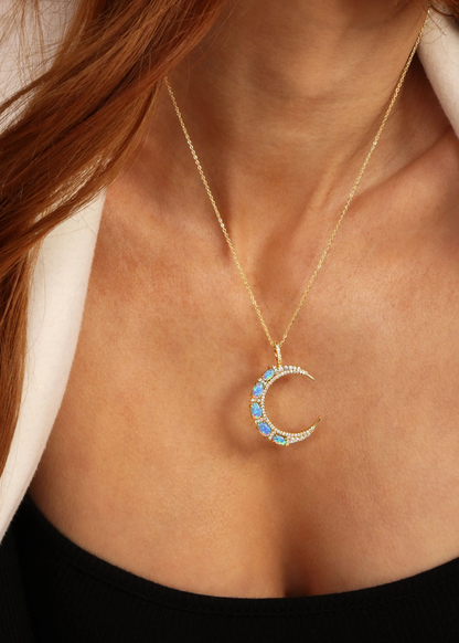 Woman wearing a gold necklace with a gold moon pendant with blue opal studs