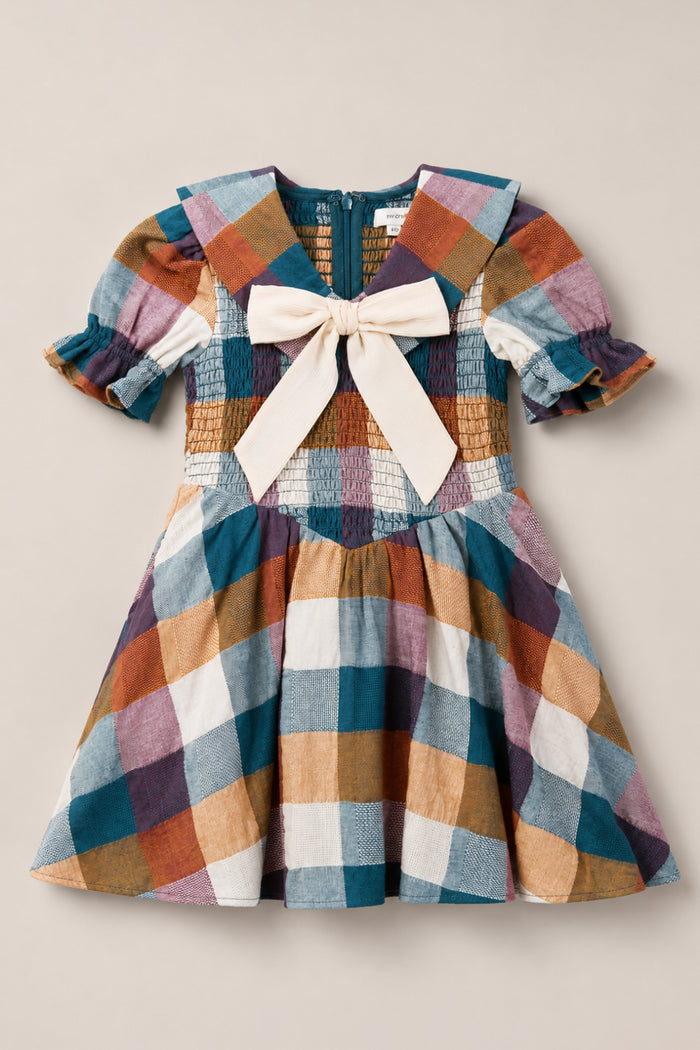 The Mini Alice Dress in Maize Gingham by Ivy City Co showcases a delightful plaid pattern in blue, white, mustard, and mauve checks. Featuring puff sleeves, a smocked bodice, sailor collar, back zipper, and a large cream bow on the front, this dress perfectly combines classic elegance with playful details.