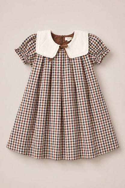 A short-sleeved Mini Emery Dress in Chestnut Gingham by Ivy City Co, featuring a large white Peter Pan collar and gathered puff sleeves, displayed flat on a light beige background—perfect as a classic girls’ cotton dress for any occasion.