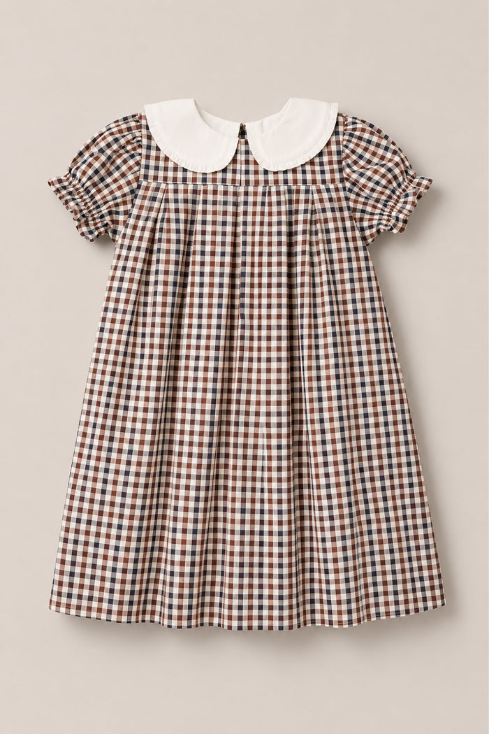 The Mini Emery Dress in Chestnut Gingham by Ivy City Co—a short-sleeve, knee-length girls' cotton dress with a brown, blue, and white plaid pattern, crisp white Peter Pan collar, and gathered sleeves—is laid flat on a light background.