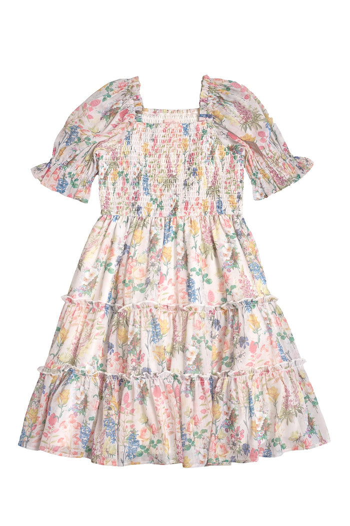 The Mini Madeline Dress in Cordelia Floral by Ivy City Co is a knee-length, short-sleeve girl’s dress with a smocked bodice and tiered ruffle skirt, showcasing a colorful floral print on white.