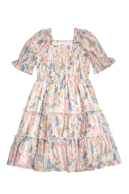 The Mini Madeline Dress in Cordelia Floral by Ivy City Co is a knee-length, short-sleeve girl’s dress with a smocked bodice and tiered ruffle skirt, showcasing a colorful floral print on white.