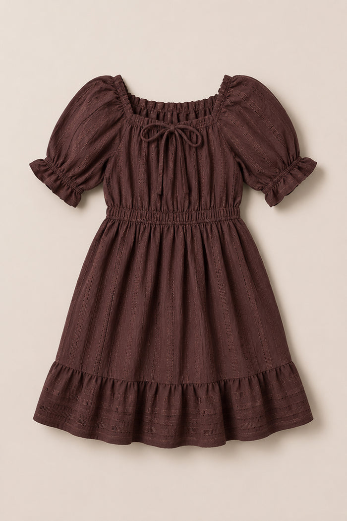 The Ivy City Co Mini Maleah Dress in Warm Cocoa is crafted from soft viscose and showcases puff sleeves, a ruffled hem, an elastic waist, and a tie at the square neckline. The dress is displayed laid flat on a light background.