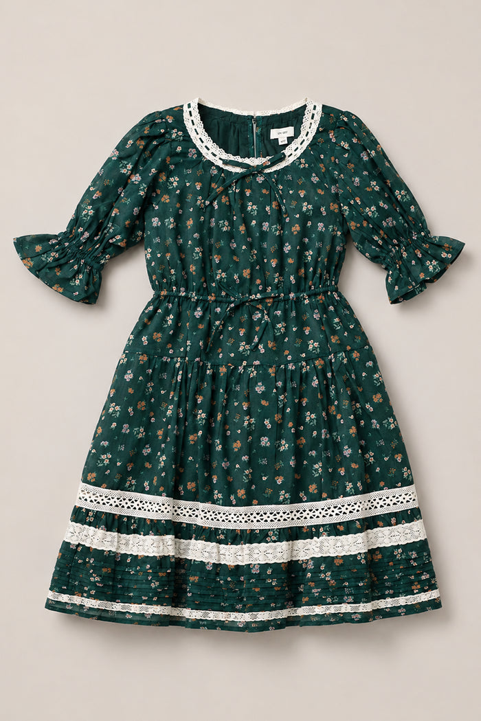 Introducing the Mini Palermo 3/4 Sleeves Dress in Evergreen Lovelorn Ditsy by Ivy City Co—a girls’ cotton dress adorned with a dark green ditsy floral print and delicate white lace accents at the neckline, cuffs, and hem. Featuring elegant 3/4 puff sleeves, a gathered waistline, and a knee-length skirt, this charming piece blends timeless florals with intricate lace details for a captivating look.