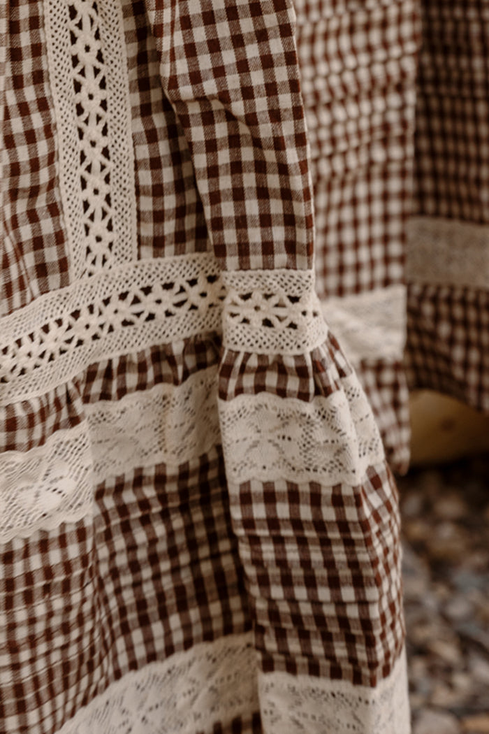 Close-up of the Mini Palermo Dress in Hickory Gingham by Ivy City Co, showcasing a brown and white gingham cotton-blend fabric with intricate white lace trim, crochet details, and puff sleeves that highlight the garment's textured patterns and expert stitching.