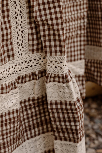 Close-up of the Mini Palermo Dress in Hickory Gingham by Ivy City Co, showcasing a brown and white gingham cotton-blend fabric with intricate white lace trim, crochet details, and puff sleeves that highlight the garment's textured patterns and expert stitching.