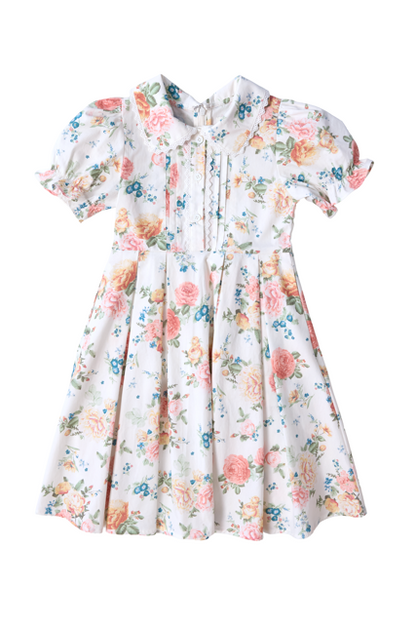 The Mini Sophia Dress in Countryside Peony Blossom by Ivy City Co is an ivory floral girls’ spring dress with pink, blue, and green blooms, short sleeves, pleated front, buttons, Peter Pan collar, fitted waist, and a full gathered skirt.