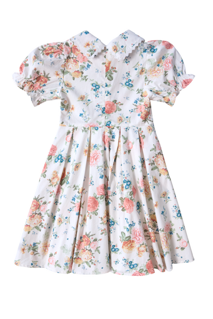 The Mini Sophia Dress in Countryside Peony Blossom by Ivy City Co is an ivory floral girls’ spring dress with pink, peach, blue, and green blooms, a pleated skirt, puffed sleeves, fitted waist, and a lace-trimmed Peter Pan collar.