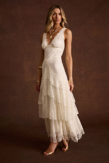 Cream lace maxi dress with V-neck and tiered ruffle skirt, styled with gold heels.
