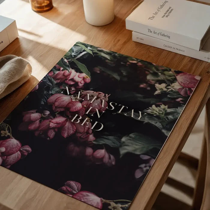 Namastay In Bed typography print on archival paper featuring dark floral botanical art on a wooden desk.