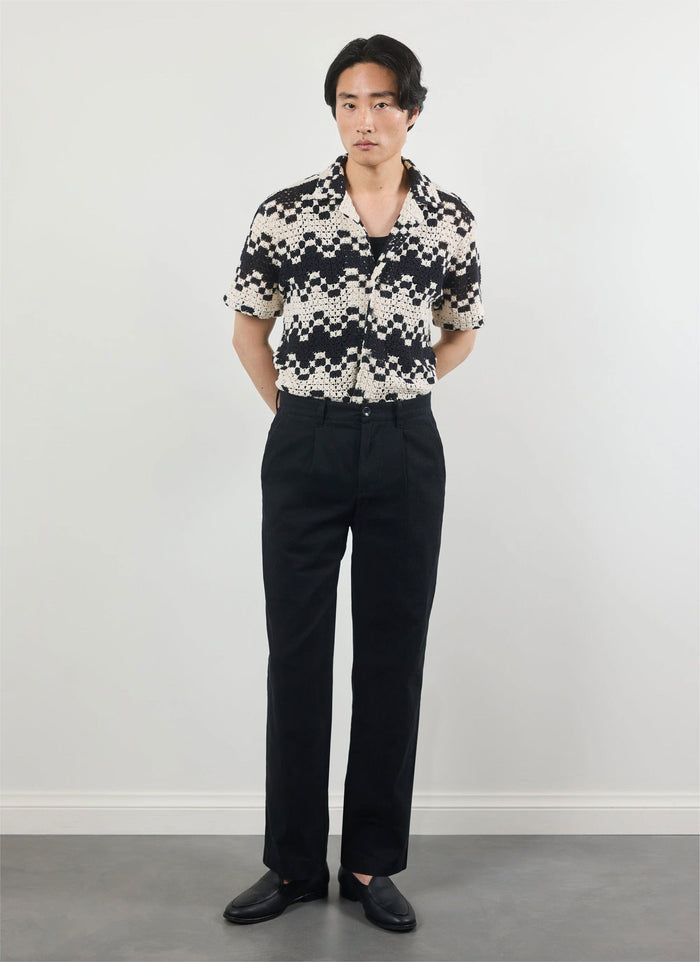 A man models the Percival Naples Crochet Cuban Shirt in ecru and black, styled with smart black trousers.