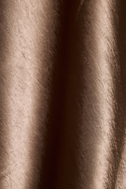 Close-up of brown satin fabric with soft draped folds.