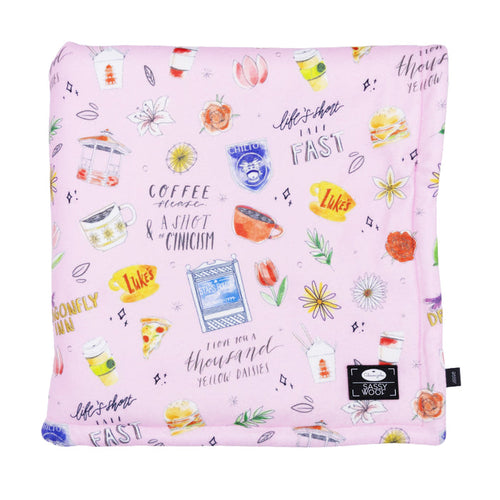 A pink Pet Blanket from the Gilmore Girls™ collection by Sassy Woof featuring colorful coffee cups, burgers, flowers, and Stars Hollow quotes like "Life is short, talk fast" and "Coffee please & a shot of cynicism.