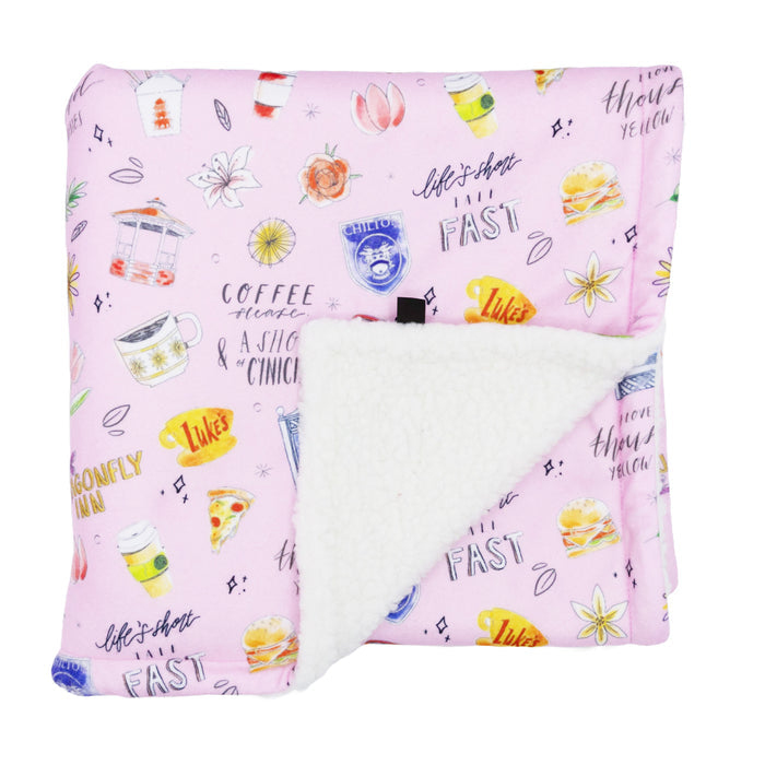 The Sassy Woof Pet Blanket - Gilmore Girls™ is a folded pink sherpa blanket with a soft white lining, decorated with coffee cups, burgers, pizza, flowers, and fun text—ideal for any Stars Hollow or Gilmore Girls fan.