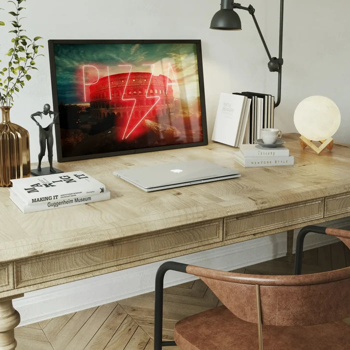 Framed glossy print of a glowing red neon Pizza sign overlaid on the Roman Colosseum, displayed on a wooden desk.