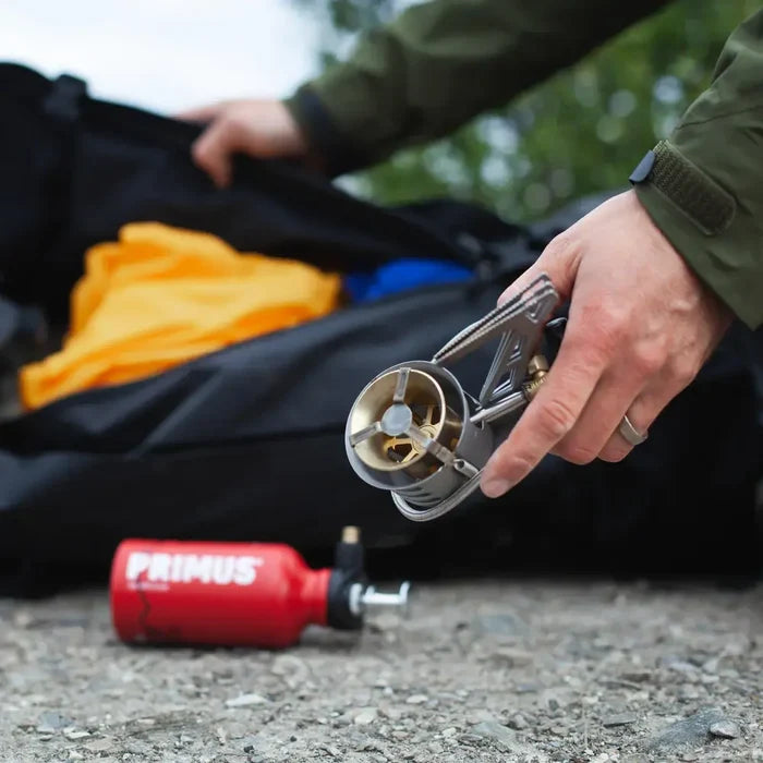 Person using a Primus Expedition Multifuel Stove with a backpack and camping gear in the background.