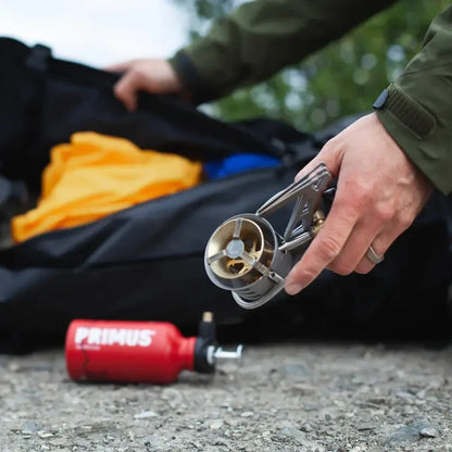 Person using a Primus Expedition Multifuel Stove with a backpack and camping gear in the background.