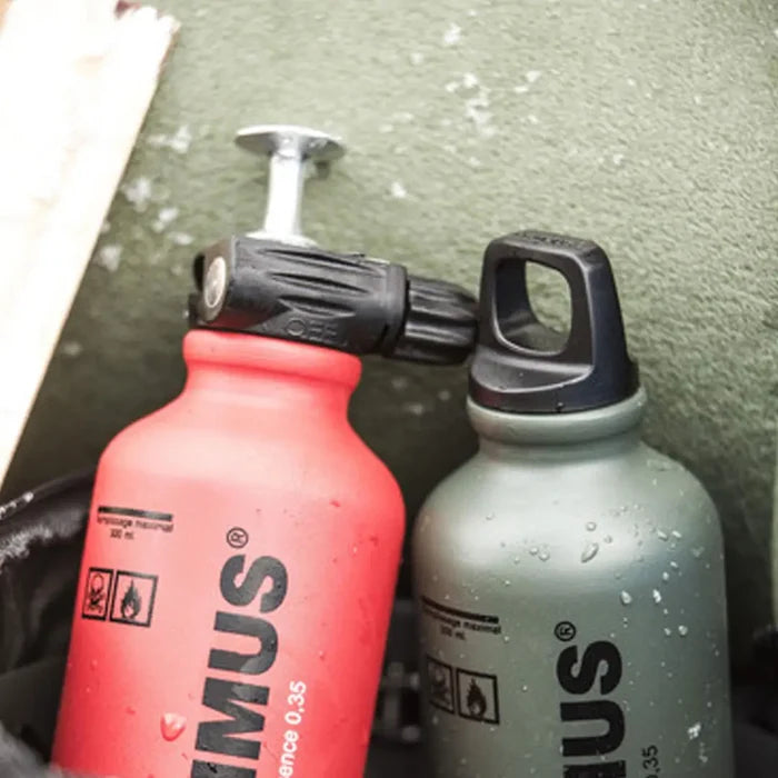 Two Primus fuel bottles, one red and one green, on a green textured surface.