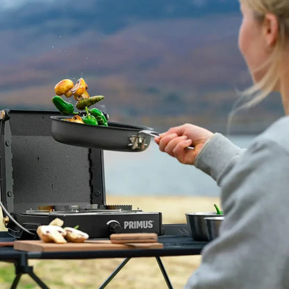 Person cooking outdoors using a small Primus Litech frying pan to cook vegetables on a Primus camping stove.