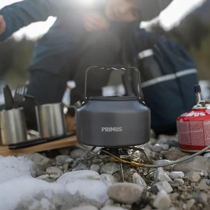 Primus Gravity camping stove with a Litech 1500ml kettle on top, nestled in rocky ground with a person in the background