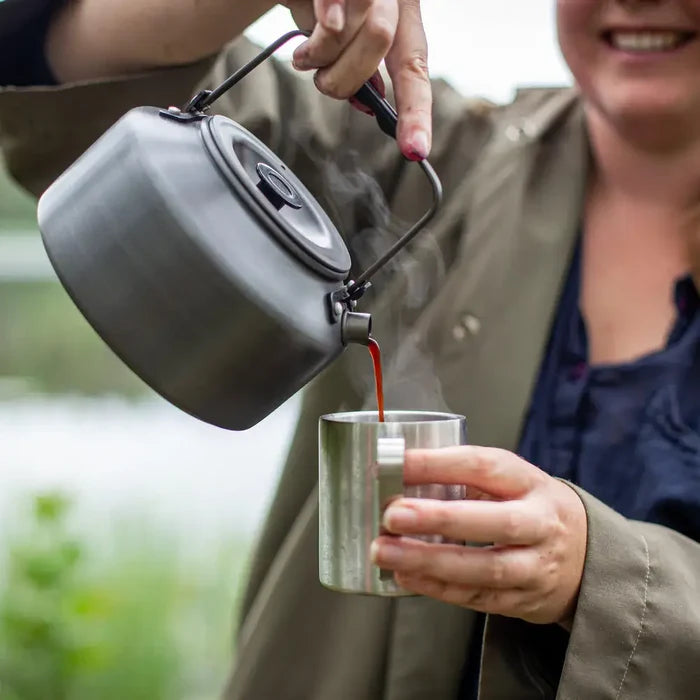 Person pouring coffee from a Primus 1500ml Litech camp kettle into a stainless steel mug outdoors.