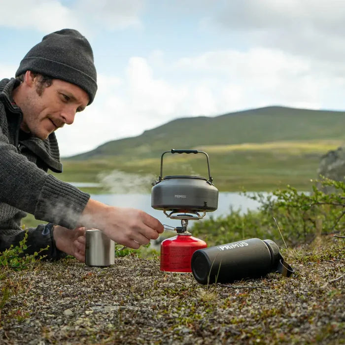 Person camping outdoors using a portable stove with a Primus 900ml Litech kettle.