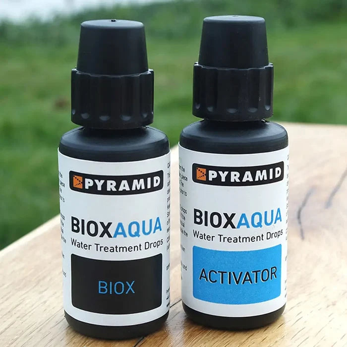 Two bottles of Pyramid BIOX Aqua water treatment drops on a wooden surface with grass in the background.