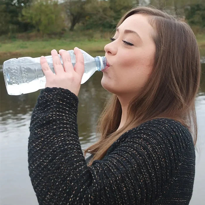 Woman drinking Pyramid Biox Aqua Chlorine Dioxide treated water from a bottle outdoors by a body of water