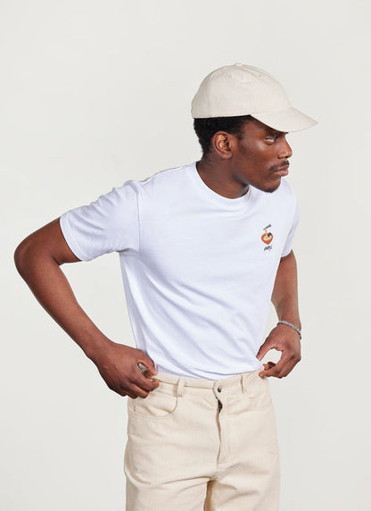 Model wears the white Percival Ramen embroidered t-shirt with cream corduroy trousers and a matching cream baseball cap.