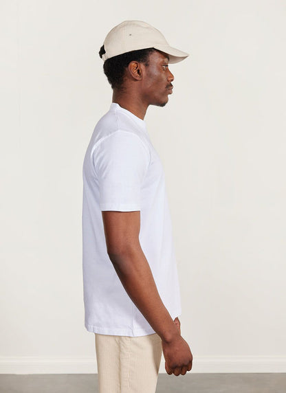 A model seen from the side wearing the white Percival Ramen T-Shirt, a cream cap and cream trousers.