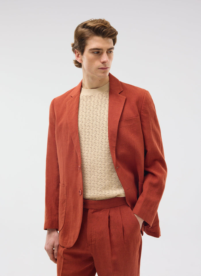 A model wears the Percival rust linen tailored blazer and matching trousers over a cream knitted sweater.