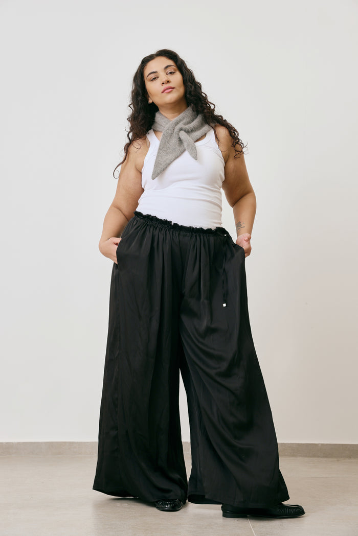 Woman wearing a white top, black wide-leg pants, and a gray scarf against a plain background