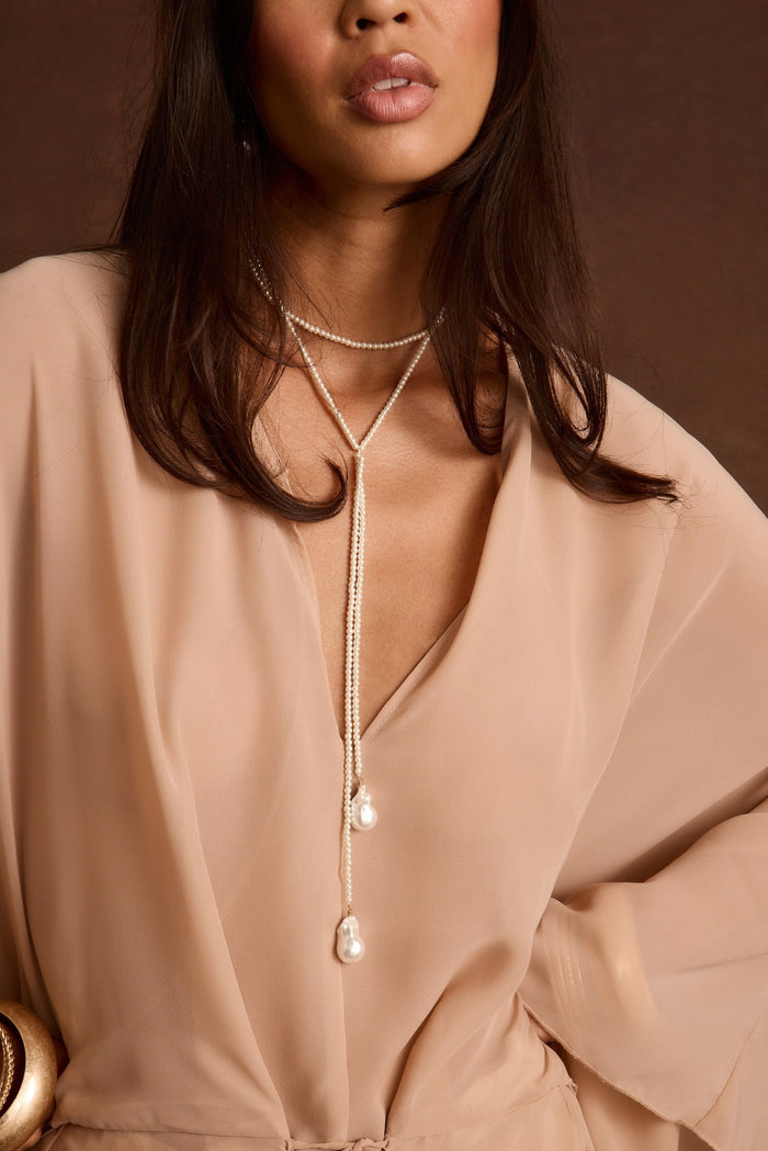 Long pearl lariat necklace with two baroque pearl drops, layered over a sheer blush blouse.