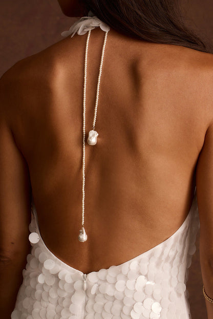 Pearl lariat necklace with a baroque pearl drop draped down the back, worn with a white sequin gown.
