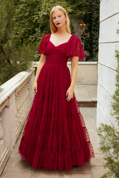 Woman in a red dress standing outdoors with greenery in the background