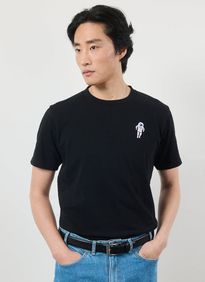 A model wears the Percival Spaceman T-Shirt in black organic cotton with blue jeans against a white studio background.