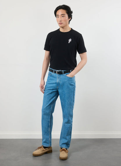 A model wears the black Percival Spaceman t-shirt, pairing it with light wash blue jeans and tan boat shoes.