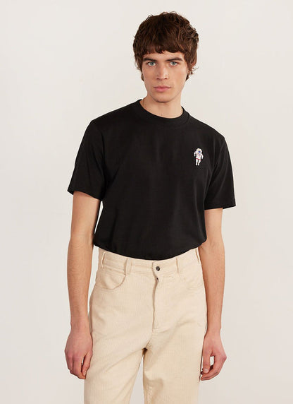 A model wears the black Percival Spaceman embroidered T-shirt with cream corduroy trousers.