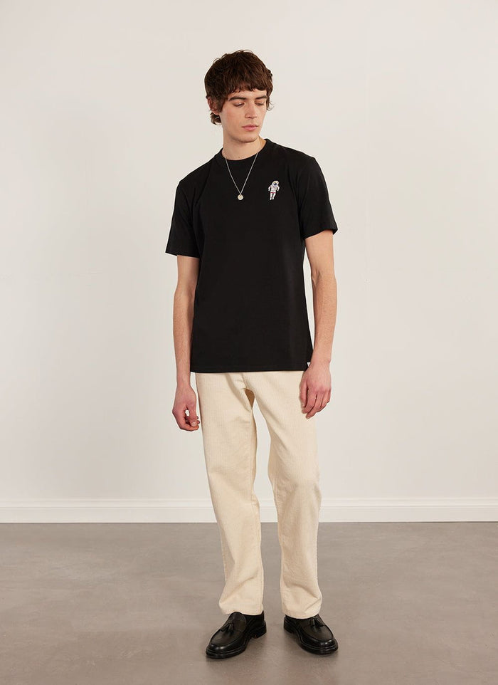 A model wears the black Percival Spaceman T-Shirt, paired with cream corduroy trousers and black loafers.