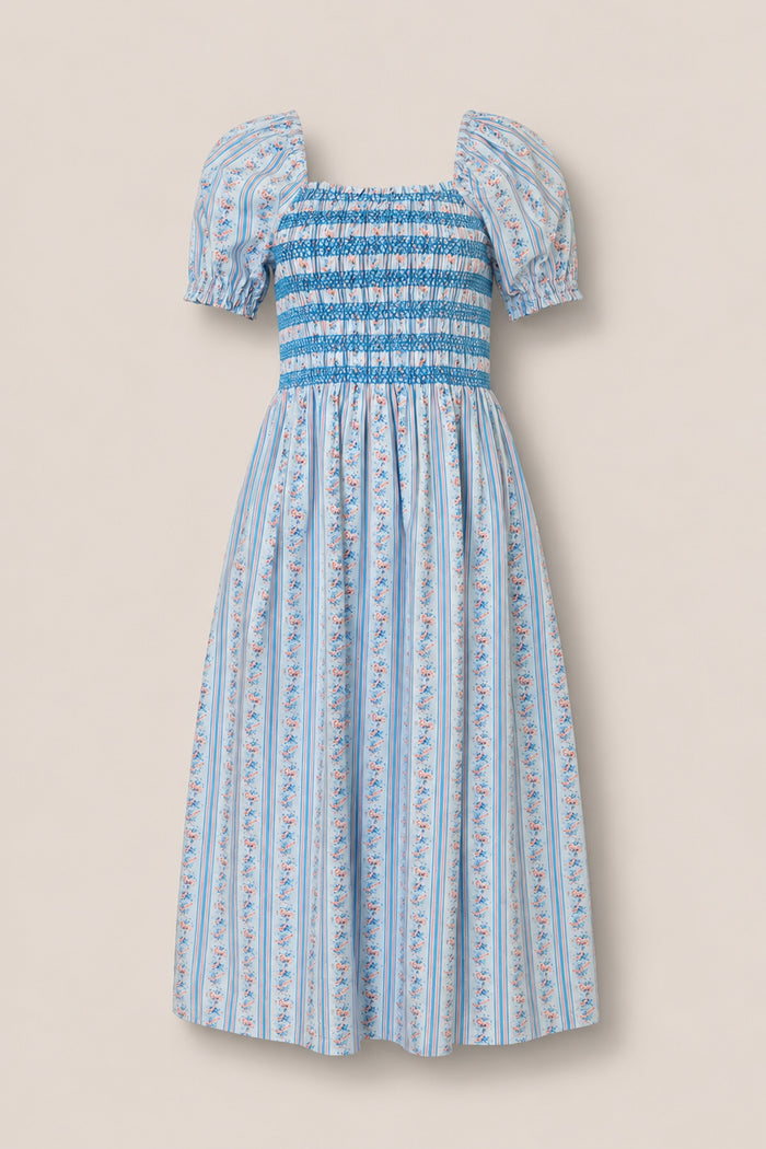 The Sunday Best Dress in Rosette Linear Stripe by Ivy City Co is a light blue, knee-length maternity dress with puffed sleeves, smocked bodice, flared skirt, vertical stripes, and pink-blue floral details for stylish comfort.