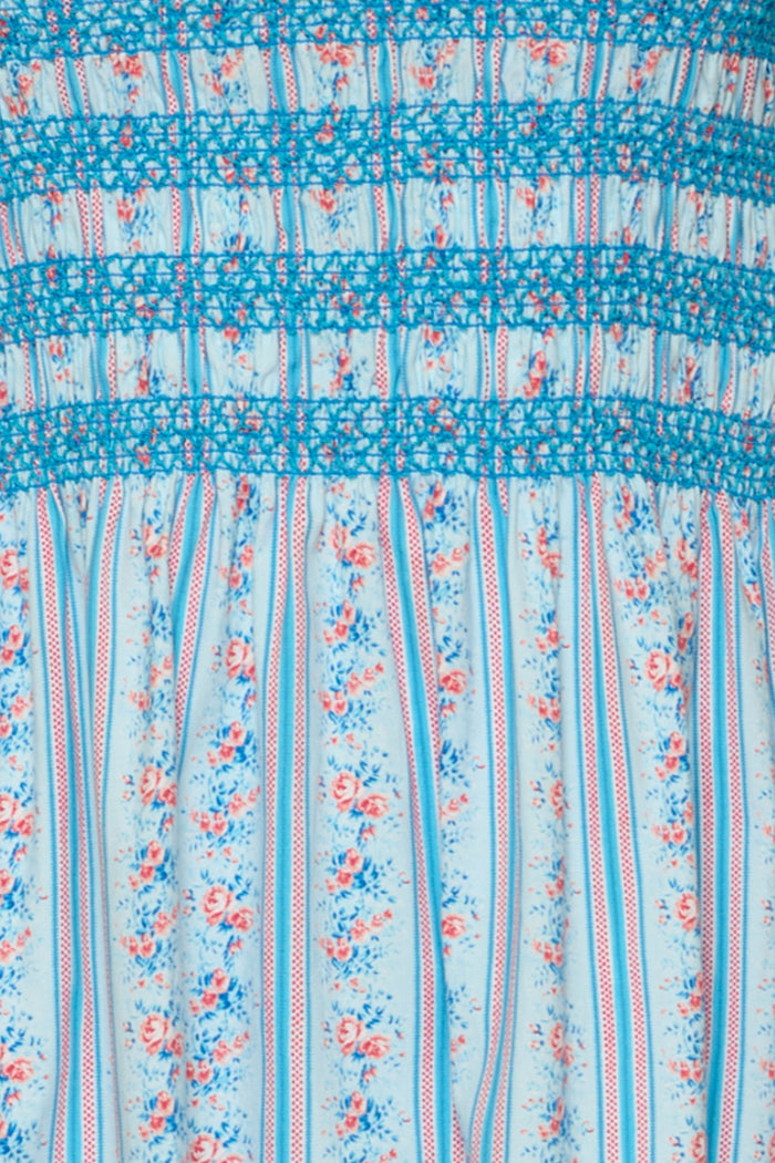 Close-up of the Sunday Best Dress in Rosette Linear Stripe by Ivy City Co: a light blue, maternity-friendly midi with pink and blue floral vertical stripes, blue thread smocking, and gathered detailing at the top.