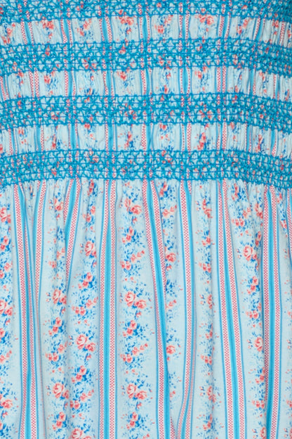 Close-up of the Sunday Best Dress in Rosette Linear Stripe by Ivy City Co: a light blue, maternity-friendly midi with pink and blue floral vertical stripes, blue thread smocking, and gathered detailing at the top.