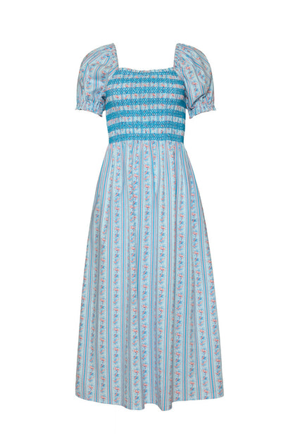 The Ivy City Co Sunday Best Dress in Rosette Linear Stripe is a light blue, ankle-length maternity-friendly dress with short puff sleeves, square neckline, blue smocked bodice, and a skirt featuring vertical stripes and florals.