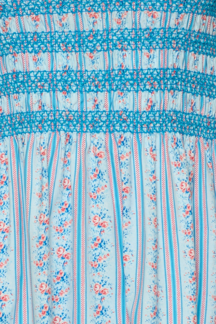 A close-up of the Ivy City Co Sunday Best Dress in Rosette Linear Stripe showcases its light blue cotton midi design with vertical red and white stripes and delicate pink floral details, finished with blue floral smocking at the top—thoughtfully crafted to be maternity friendly for easy, effortless summer style.